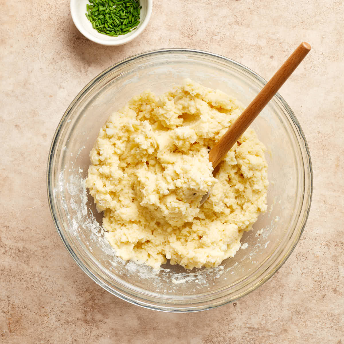 Mashed potato mixture in a bowl with a spatula and chopped chives on the side.