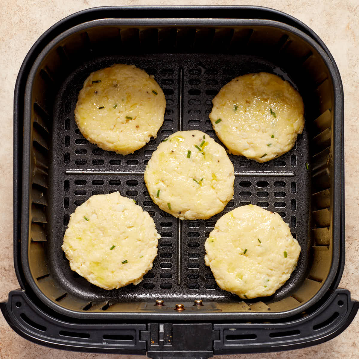Uncooked potato cakes in an air fryer basket.