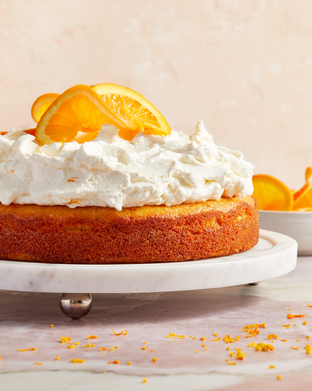 Side view of orange cake topped with whipped cream and orange slices on a white cake plate.