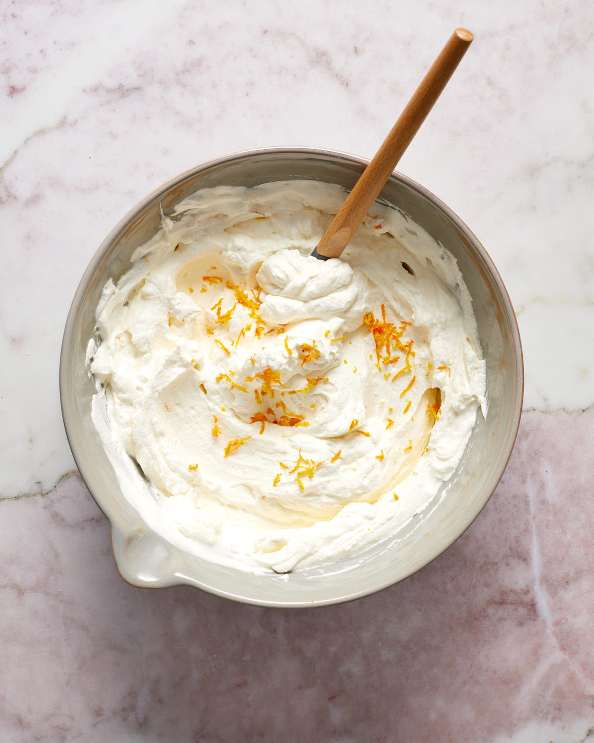 Whipped cream topping in a grey bowl with a spatula stirring in orange zest.