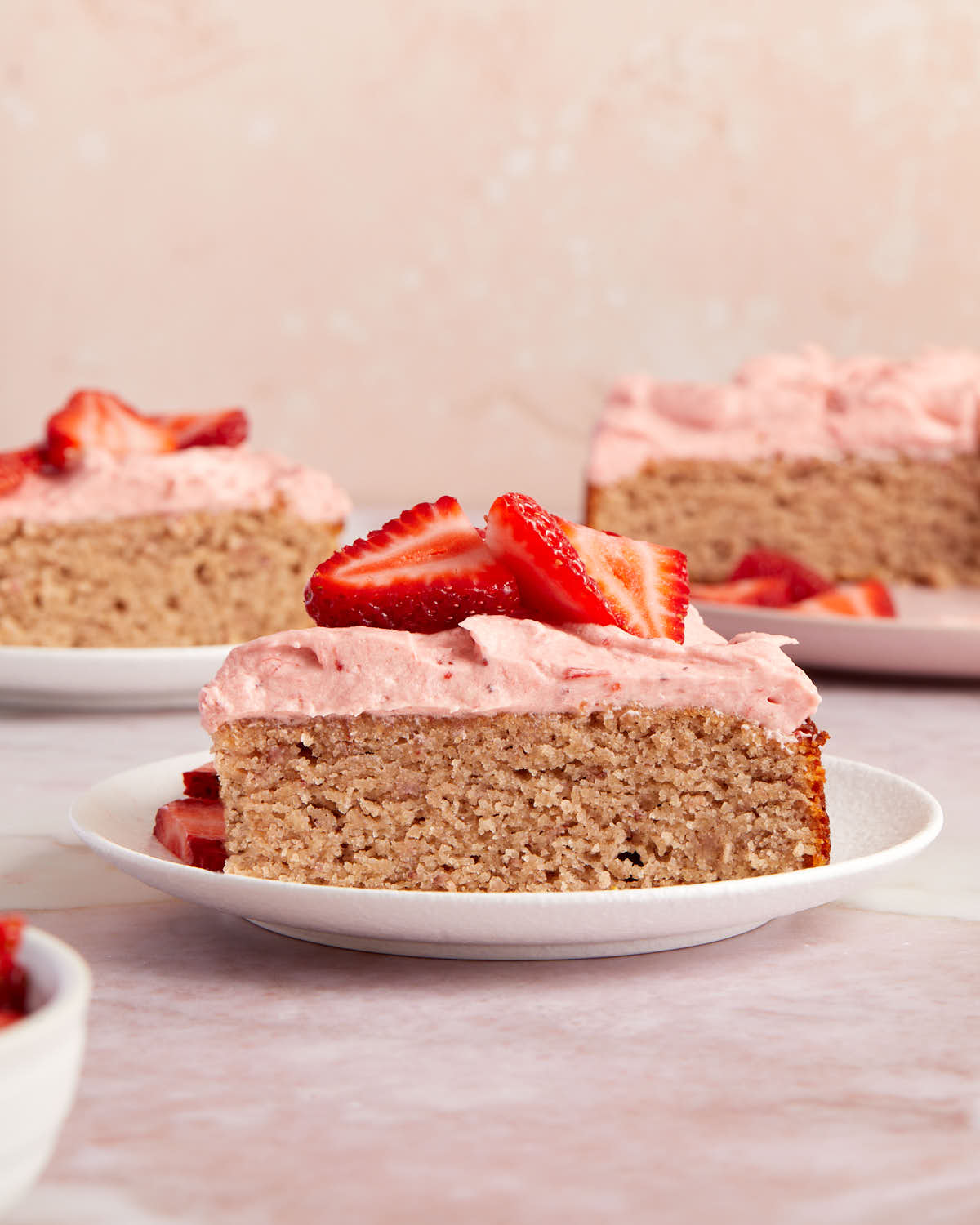 Side view of a slice of strawberry cake on a white plate and topped with fresh strawberries.