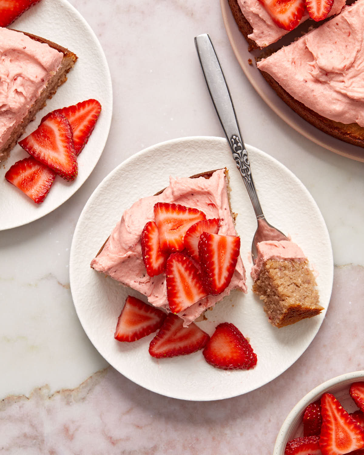 Overhead view of a slice of cake topped with strawberries and a fork removing a bite.