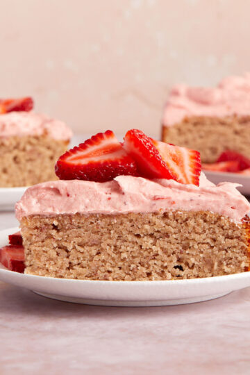 Side view of a slice of almond flour strawberry cake on a white plate with pieces of cake in the background.