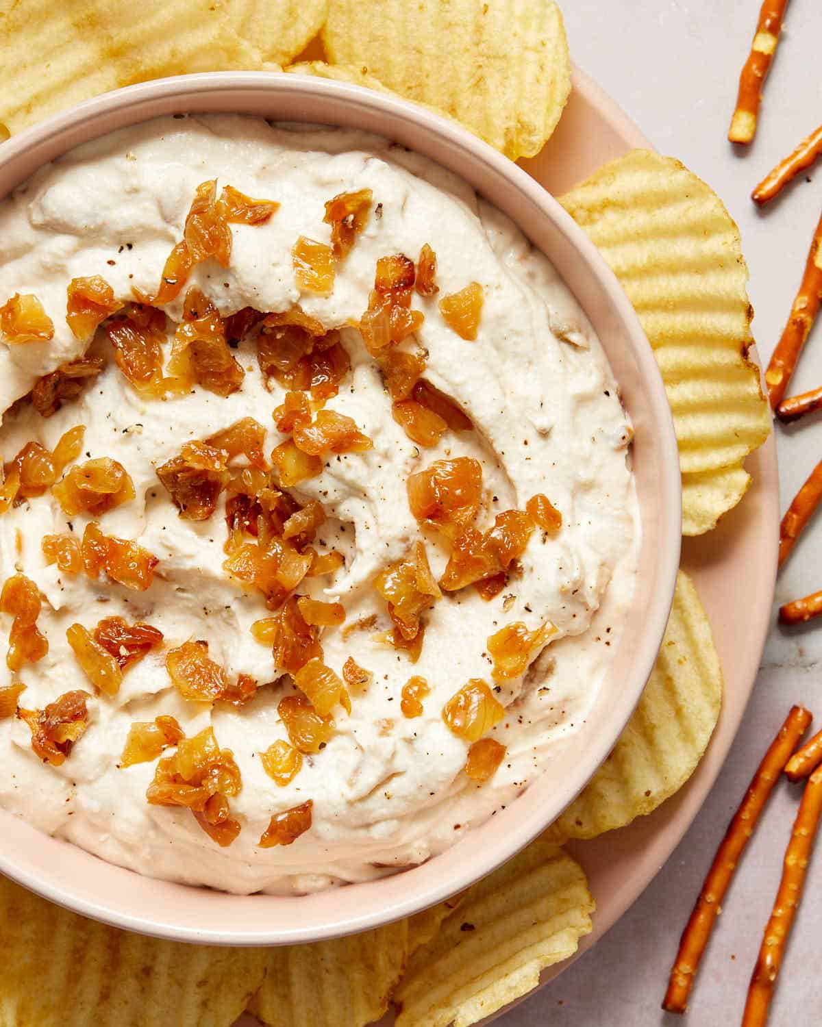 Overhead view of onion dip in a bowl with chips and pretzels on the side.