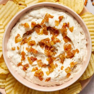 Dairy-free caramelized onion dip in a bowl with more caramelized onions on top and potato chips on the side.