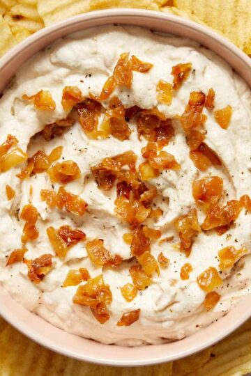 Dairy-free caramelized onion dip in a bowl with more caramelized onions on top and potato chips on the side.