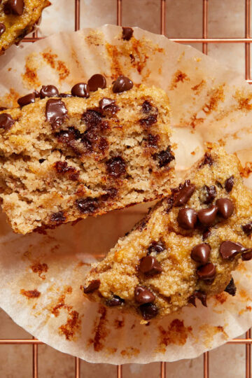 An almond flour banana muffin cut in half and resting on the muffin wrapper on a wire cooling rack.