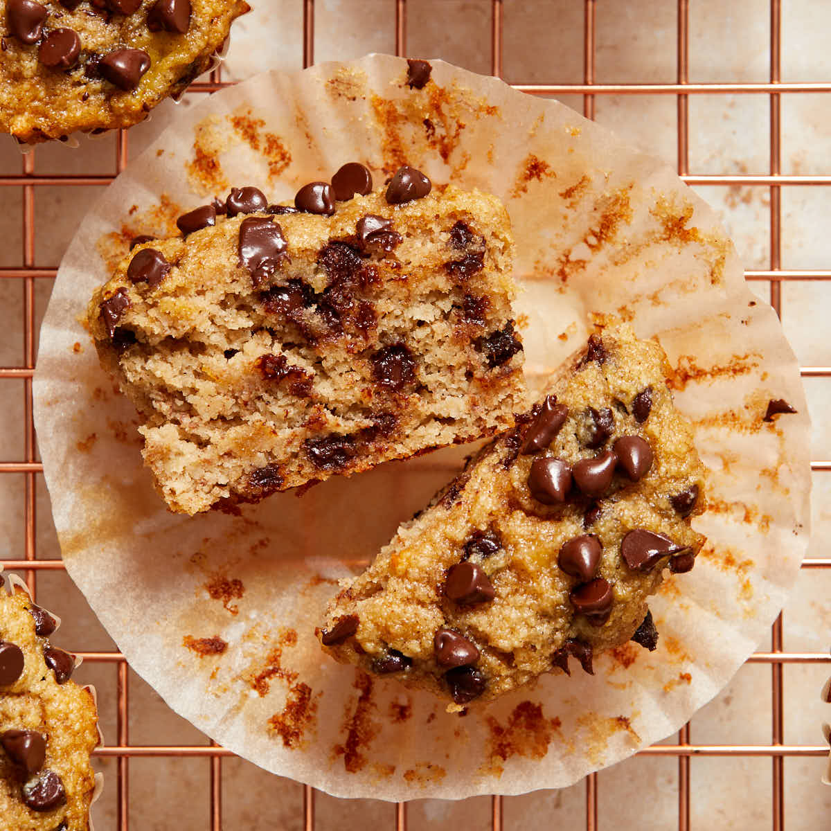 An almond flour banana muffin cut in half and resting on the muffin wrapper on a wire cooling rack.