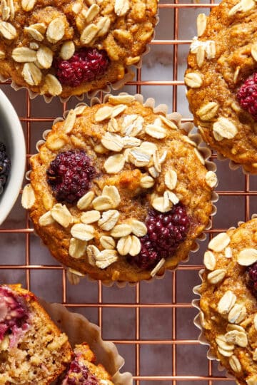 Overhead view of banana blackberry oatmeal muffins on a gold coloured wire rack.