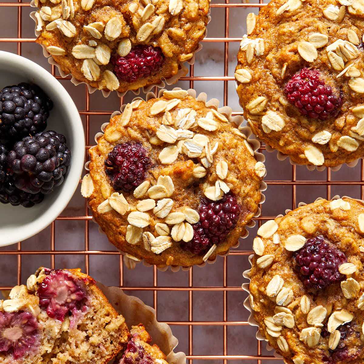 Overhead view of banana blackberry oatmeal muffins on a gold coloured wire rack.