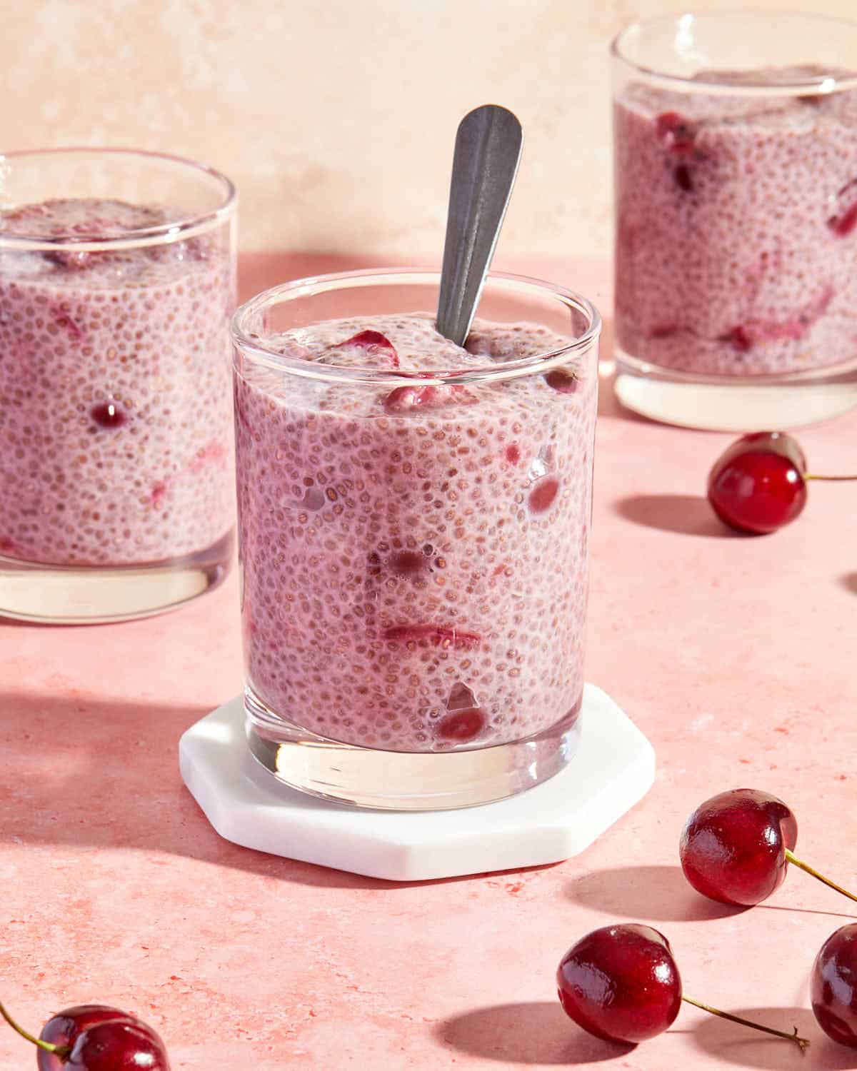 Side view of cherry chia pudding served in glasses on a pink backdrop.