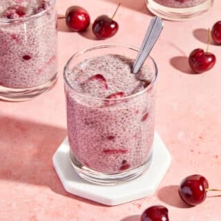 Cherry chia pudding served in a glass on a white coaster with a spoon inserted into the pudding.