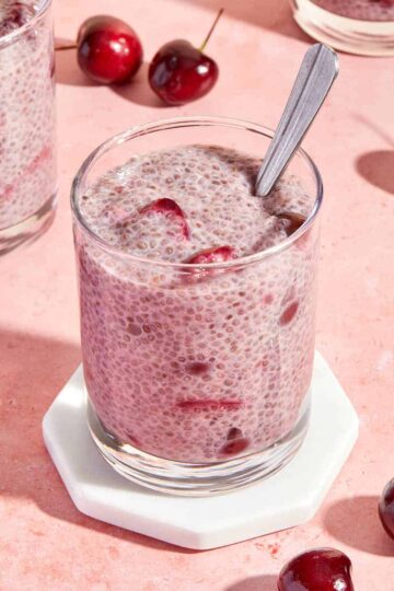 Cherry chia pudding served in a glass on a white coaster with a spoon inserted into the pudding.
