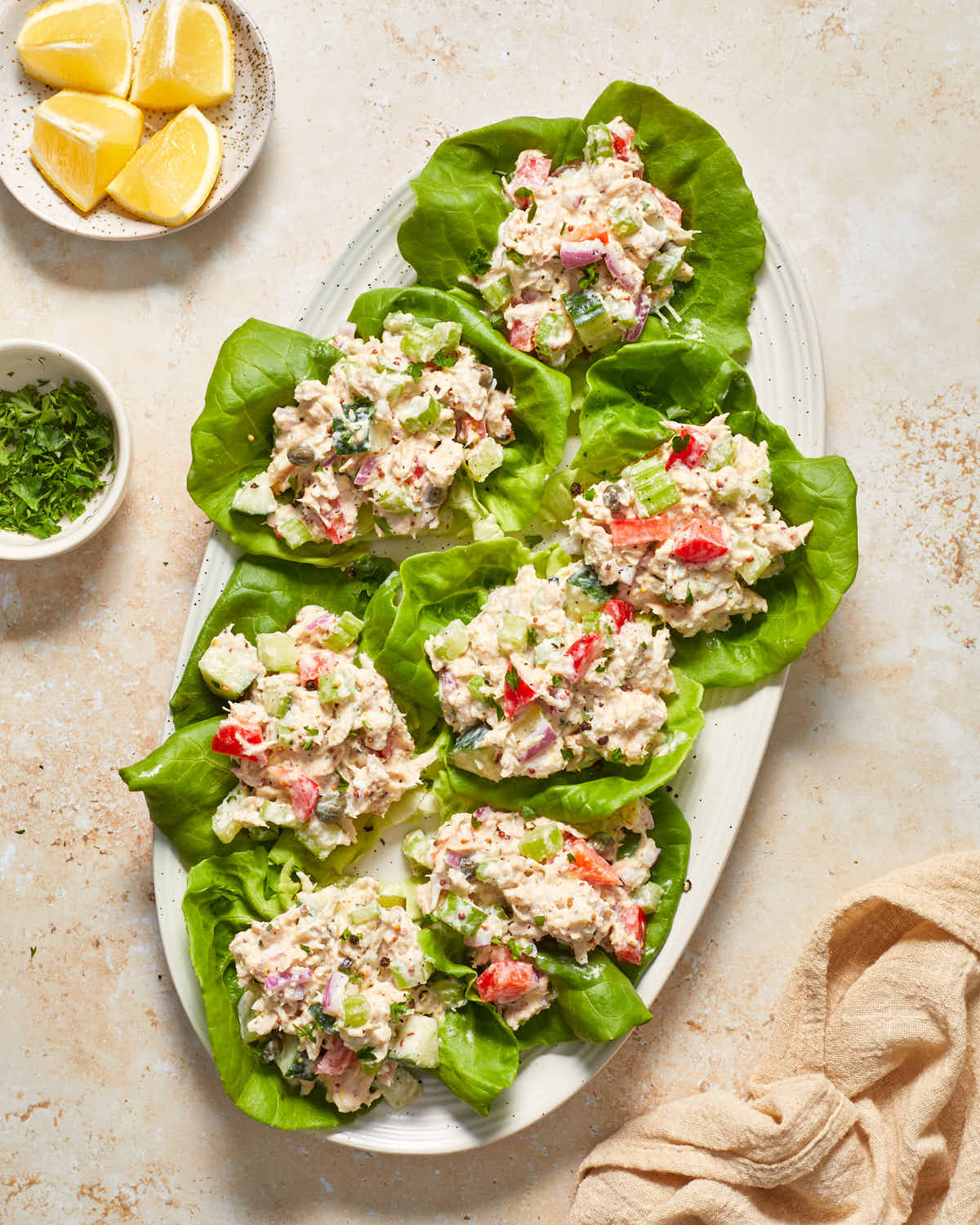 Tuna lettuce wraps arranged on an oval platter with lemons and chopped herbs on the side.