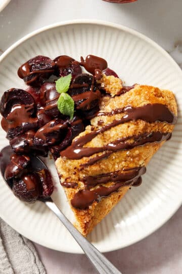 A slice of cherry galette topped with melted chocolate and served on a white plate.