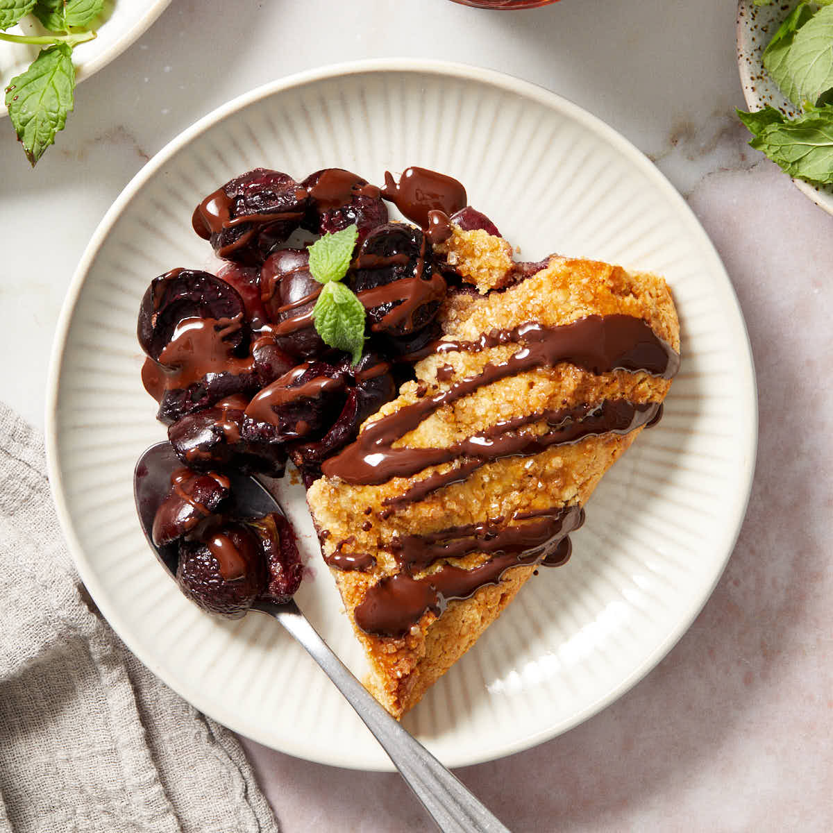 A slice of cherry galette topped with melted chocolate and served on a white plate.