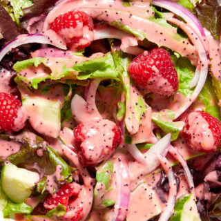 Close up view of raspberry poppy seed dressing drizzled over a salad with raspberries on top.