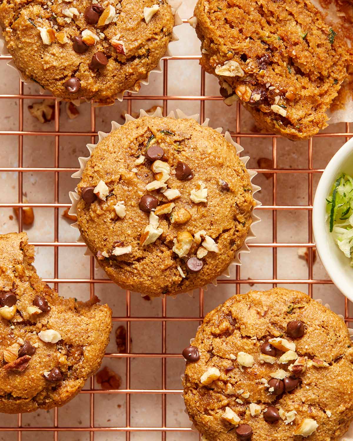 Zucchini muffins topped with chocolate chips and pecans and cooling on a wire rack.