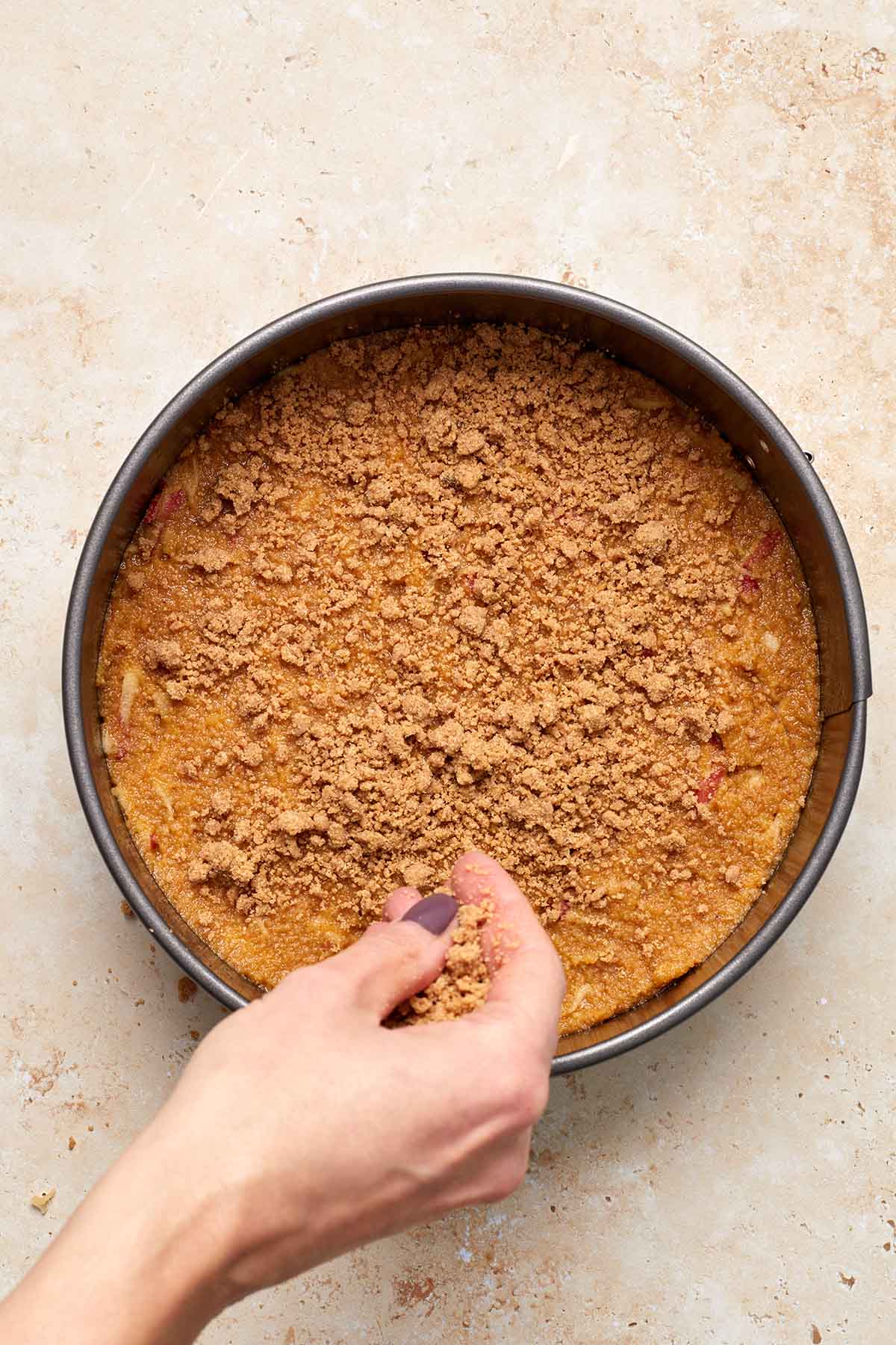 Streusel topping being scattered on top of cake batter in pan.
