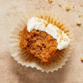 Gluten-free carrot cake cupcake on a cupcake liner with a bite taken out.