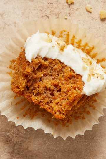 Gluten-free carrot cake cupcake on a cupcake liner with a bite taken out.