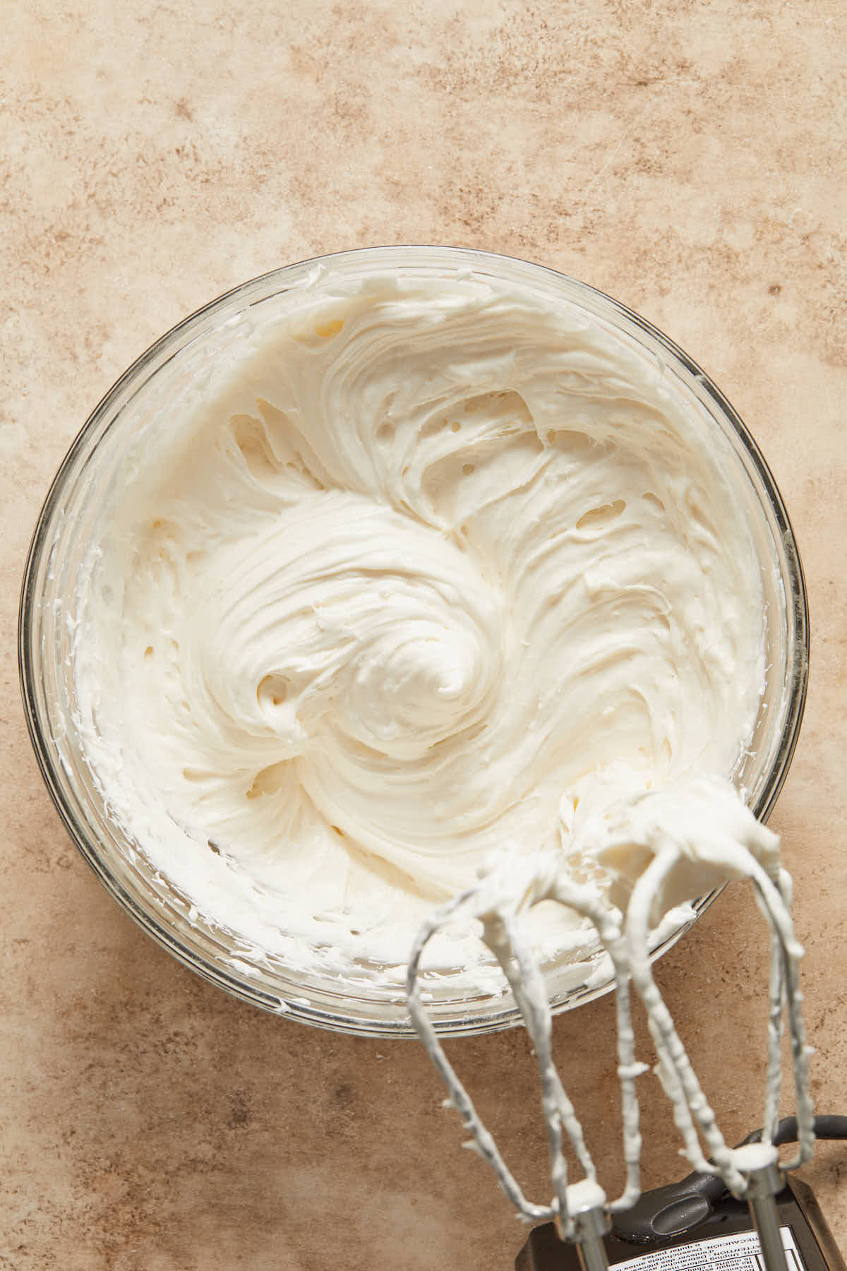 Cream cheese frosting in a glass bowl with beaters next to it.