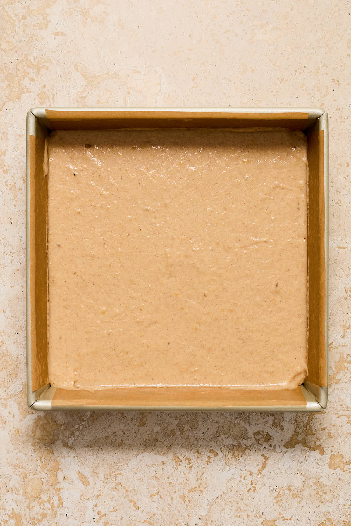 Cake batter spread out in a parchment paper lined pan.