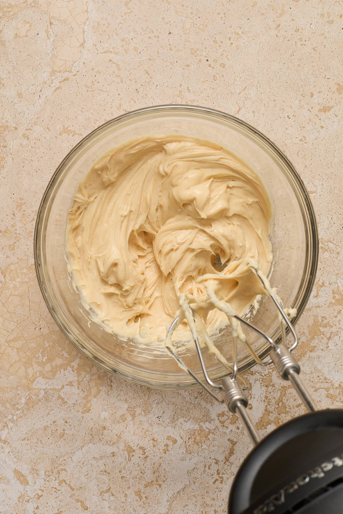 Frosting whipped together in a glass bowl with electric beaters.