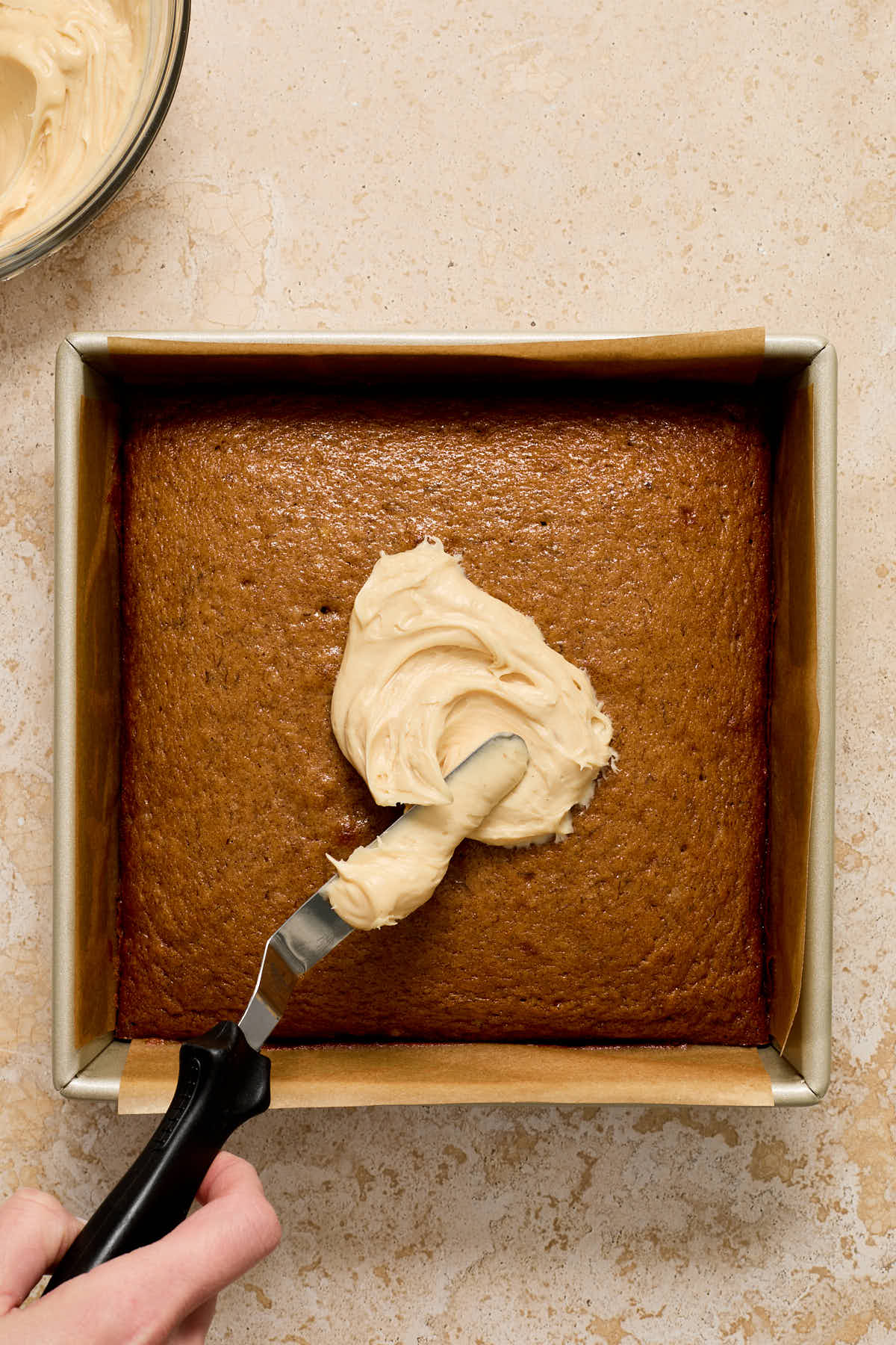 Frosting being spread onto cake with offset spatula.