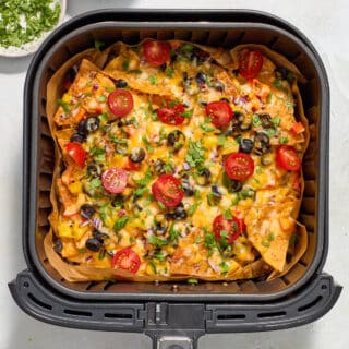Air fried nachos in the air fryer basket and topped with cherry tomatoes and chopped cilantro.