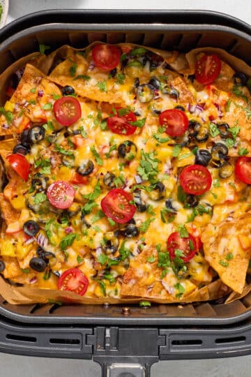 Air fried nachos in the air fryer basket and topped with cherry tomatoes and chopped cilantro.