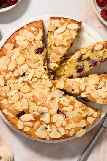 Overhead view of cherry almond cake on a cake plate with some slices cut out.
