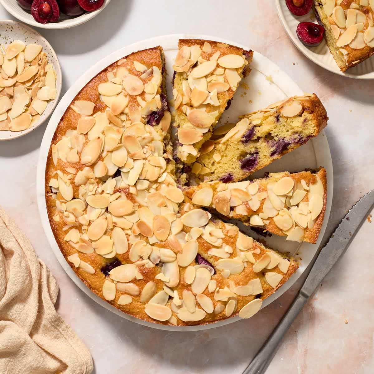 Overhead view of cherry almond cake on a cake plate with some slices cut out.
