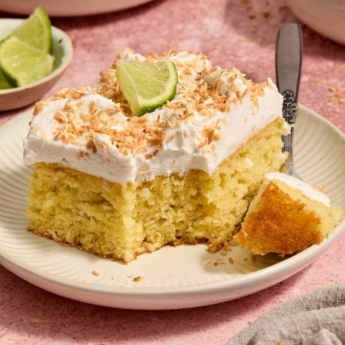 Piece of almond flour coconut lime cake on a plate with a forkful removed.
