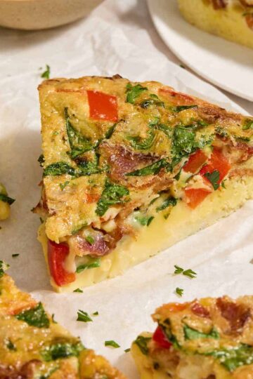 Close up view of a slice of air fryer frittata on white parchment paper.