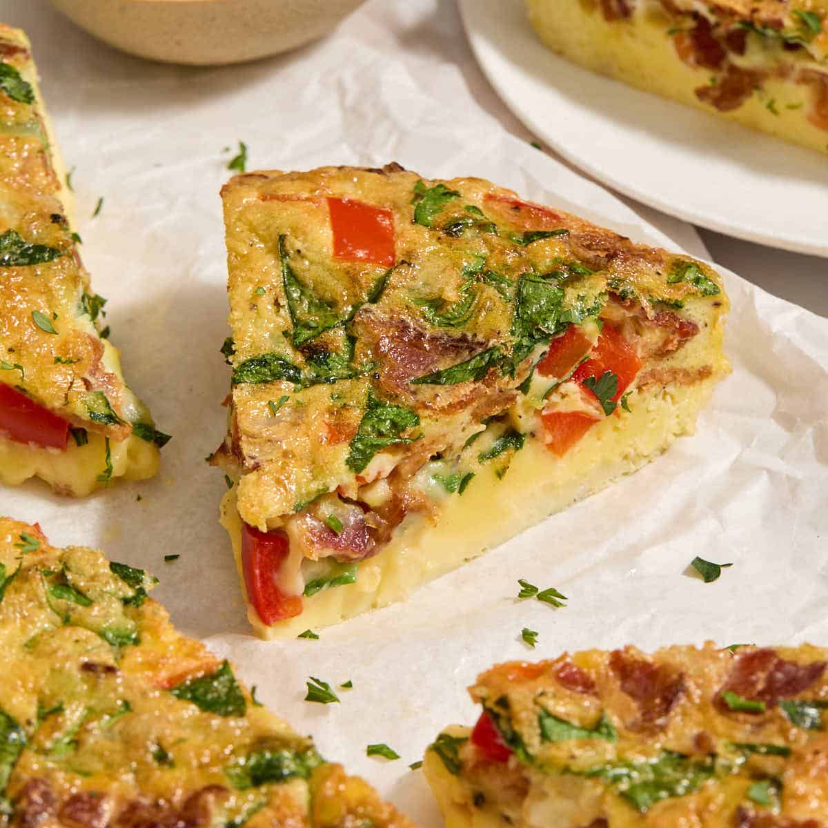 Close up view of a slice of air fryer frittata on white parchment paper.