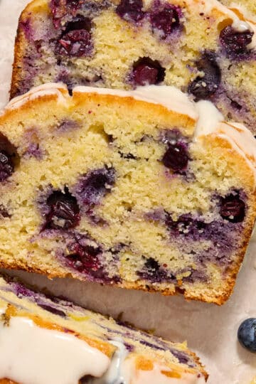 Slices of almond flour lemon blueberry bread topped with glaze and arranged on white parchment paper.