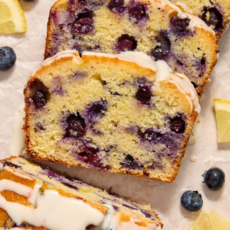 Slices of almond flour lemon blueberry bread topped with glaze and arranged on white parchment paper.