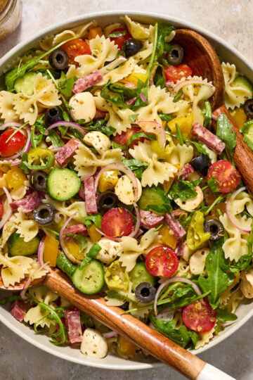 Italian bow tie pasta salad in a large bowl with wooden salad servers.