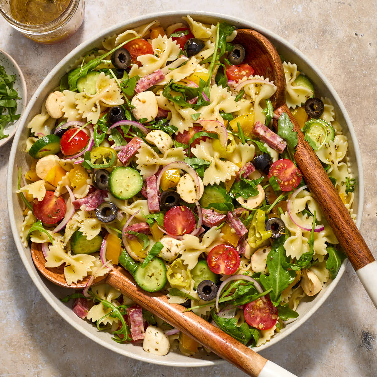 Italian bow tie pasta salad in a large bowl with wooden salad servers.