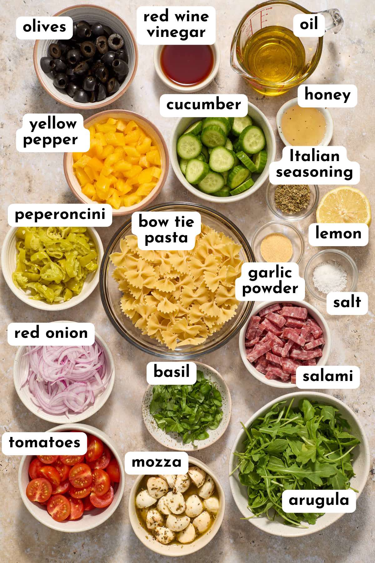 Ingredients to make an Italian bow tie pasta salad arranged individually and labeled.