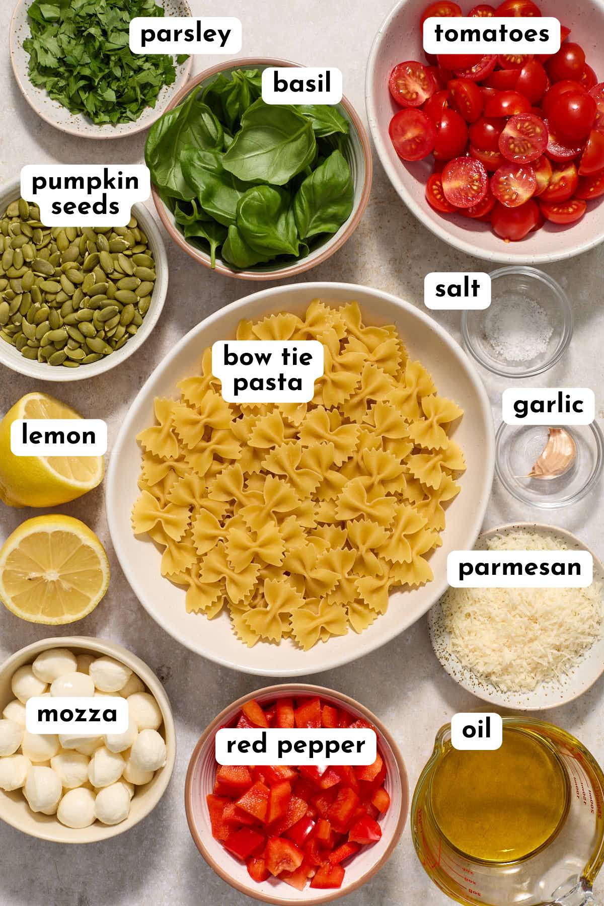 Ingredients to make a bow tie pesto pasta salad arranged individually and labeled.
