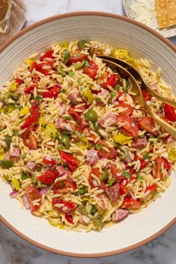 Italian orzo salad in a bowl with Italian dressing, parmesan cheese and chopped herbs on the side.
