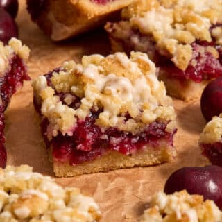 Close up side view of almond flour cherry pie bars arranged on brown parchment paper.