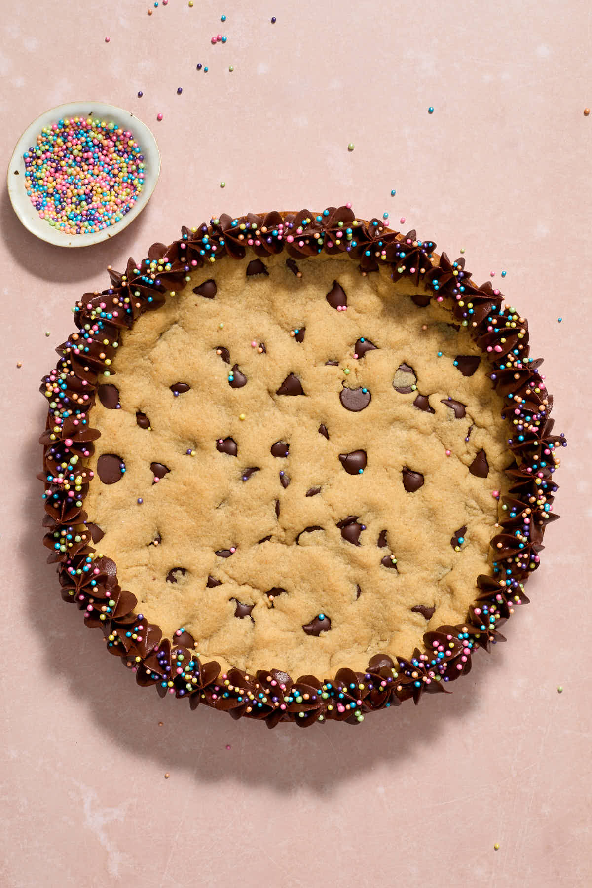 Frosting piped around the edges of the cookie cake with sprinkles on the side.