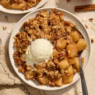 Almond flour apple pecan crisp served on a plate with a spoon and scoop of ice cream.