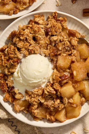 Almond flour apple pecan crisp served on a plate with a spoon and scoop of ice cream.
