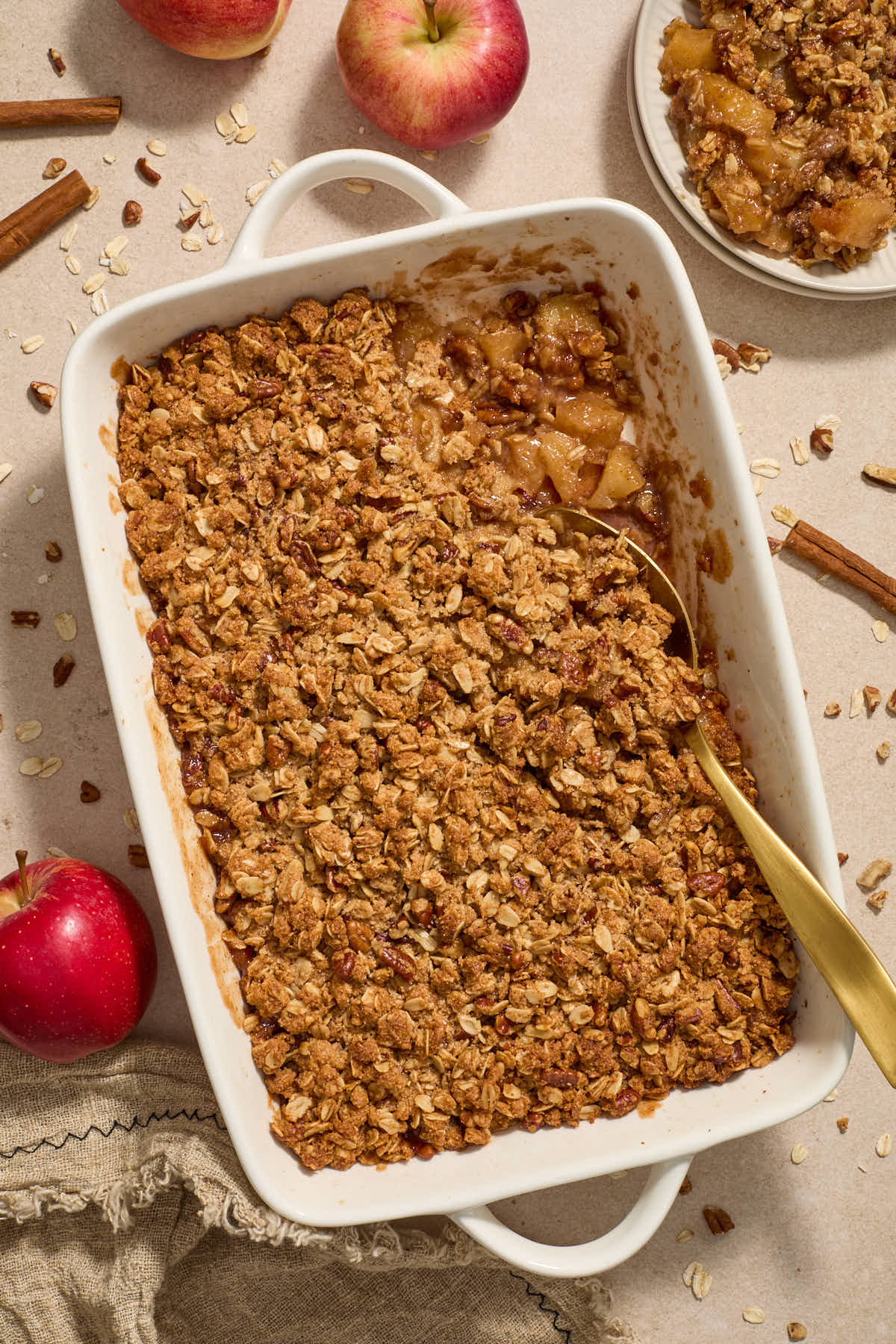 Apple crisp in baking dish with serving spoon and some scooped out on a plate to the side.