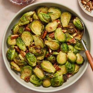 Air fryer maple pecan Brussels sprouts served in a grey bowl with a serving spoon.