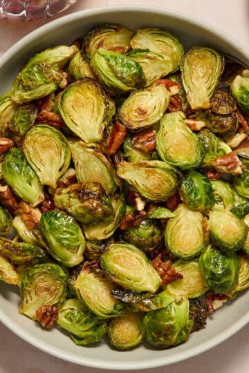 Air fryer maple pecan Brussels sprouts served in a grey bowl with a serving spoon.
